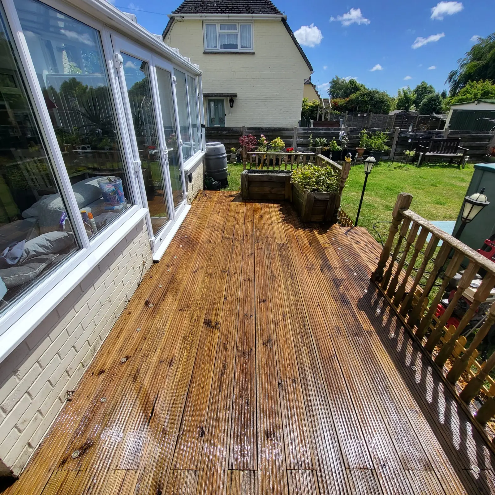 Timber decking beside a conservatory after cleaning and treatment, the boards even and rich